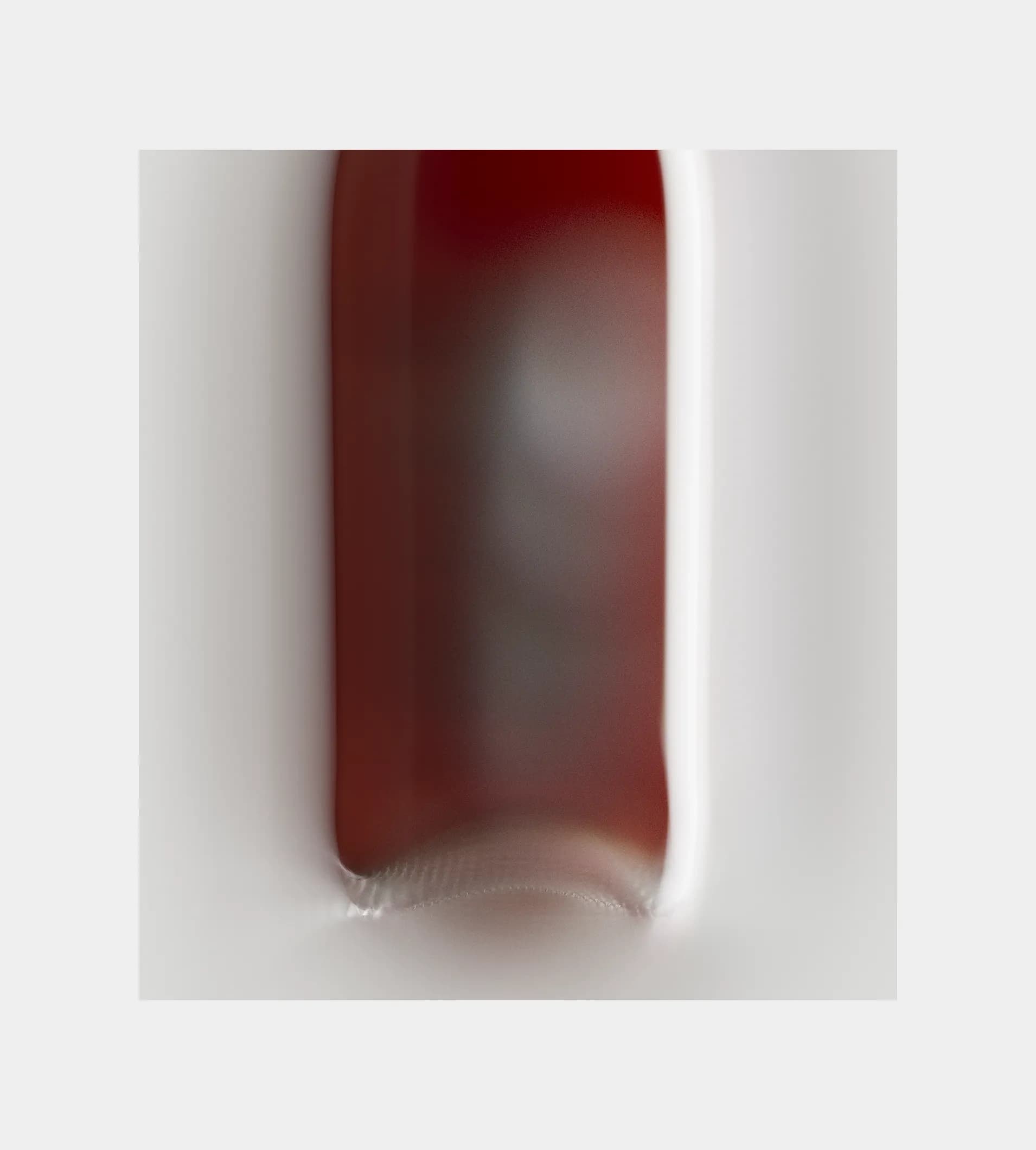 Extreme close-up of a dark red Shwung bottle, shot against a light grey background.