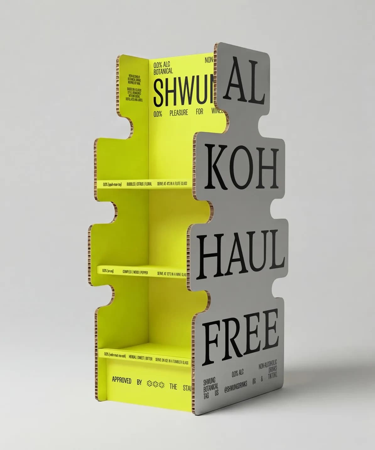 Shwung point-of-sale display unit in the die-cut label shape, made from corrugated cardboard in yellow-green and grey, with "AL KOH HAUL FREE" printed across the front in large type.