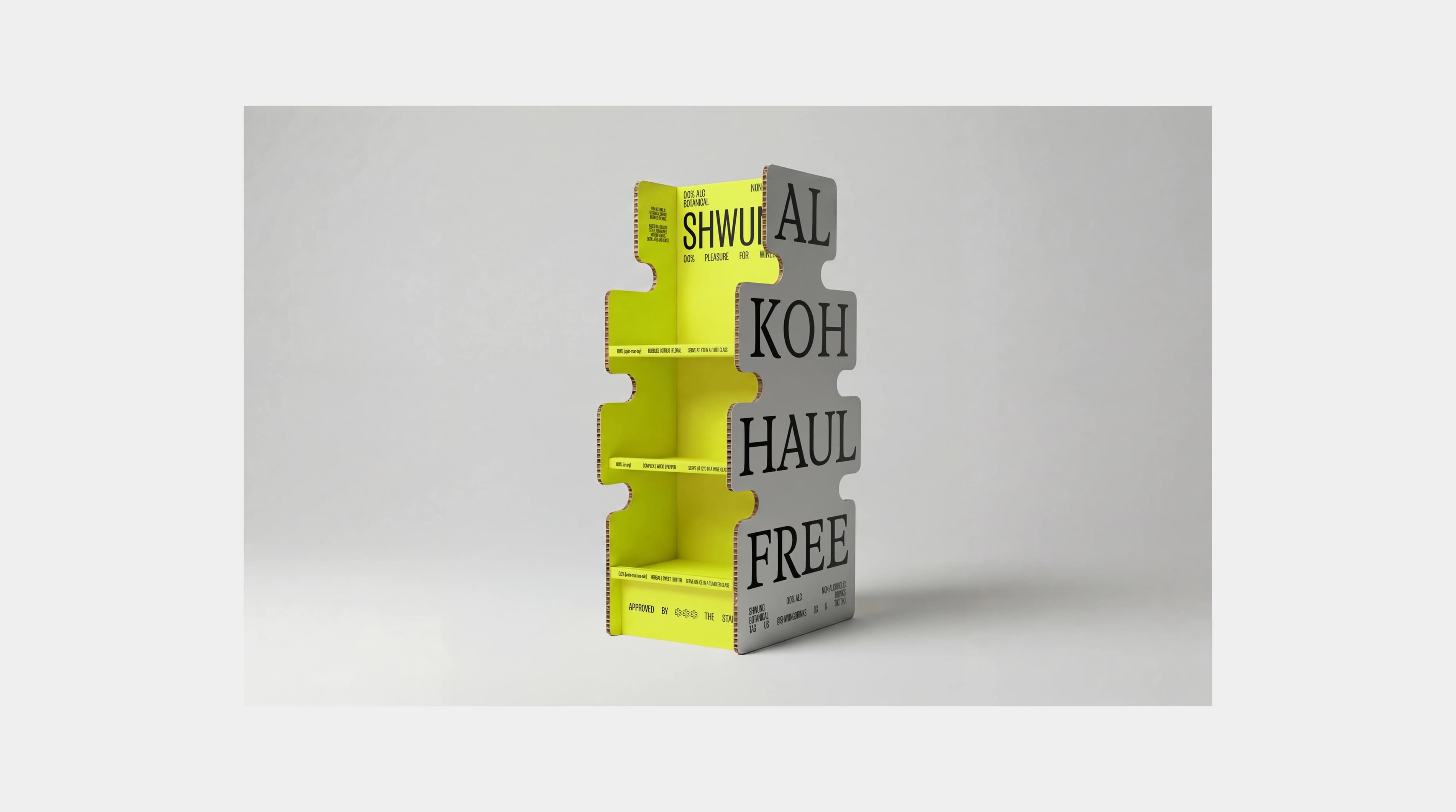 Shwung point-of-sale display unit in the die-cut label shape, made from corrugated cardboard in yellow-green and grey, with "AL KOH HAUL FREE" printed across the front in large type.