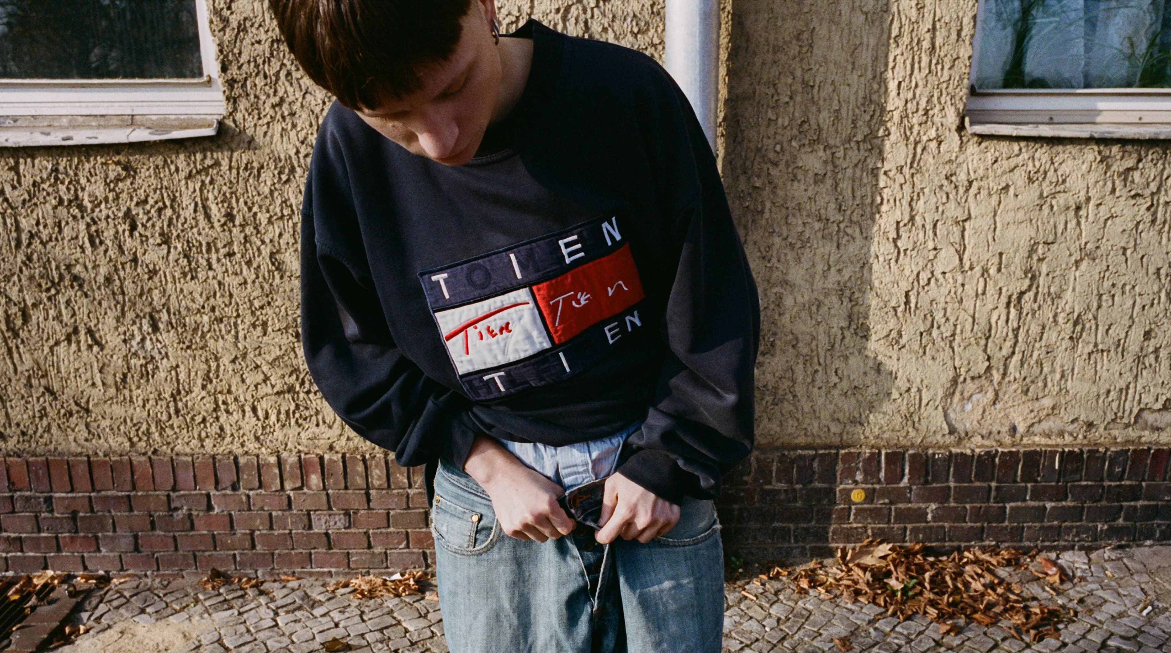 Person wearing a vintage Tommy Hilfiger sweatshirt with the original logo reworked to read TIEN, replacing the brand name while keeping the flag graphic and colorblock layout intact.
