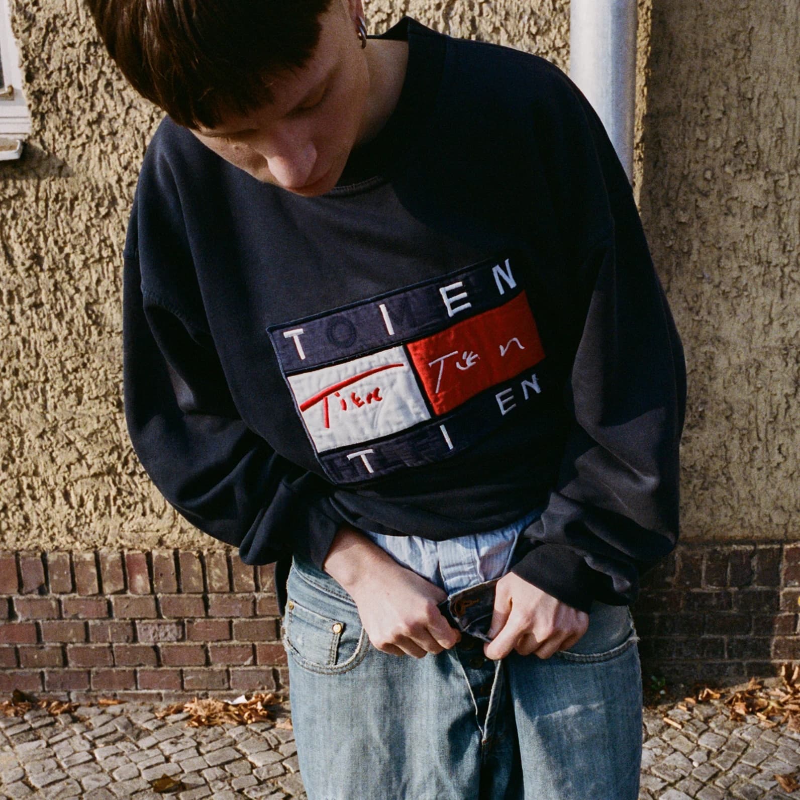 Person wearing a vintage Tommy Hilfiger sweatshirt with the original logo reworked to read TIEN, replacing the brand name while keeping the flag graphic and colorblock layout intact.