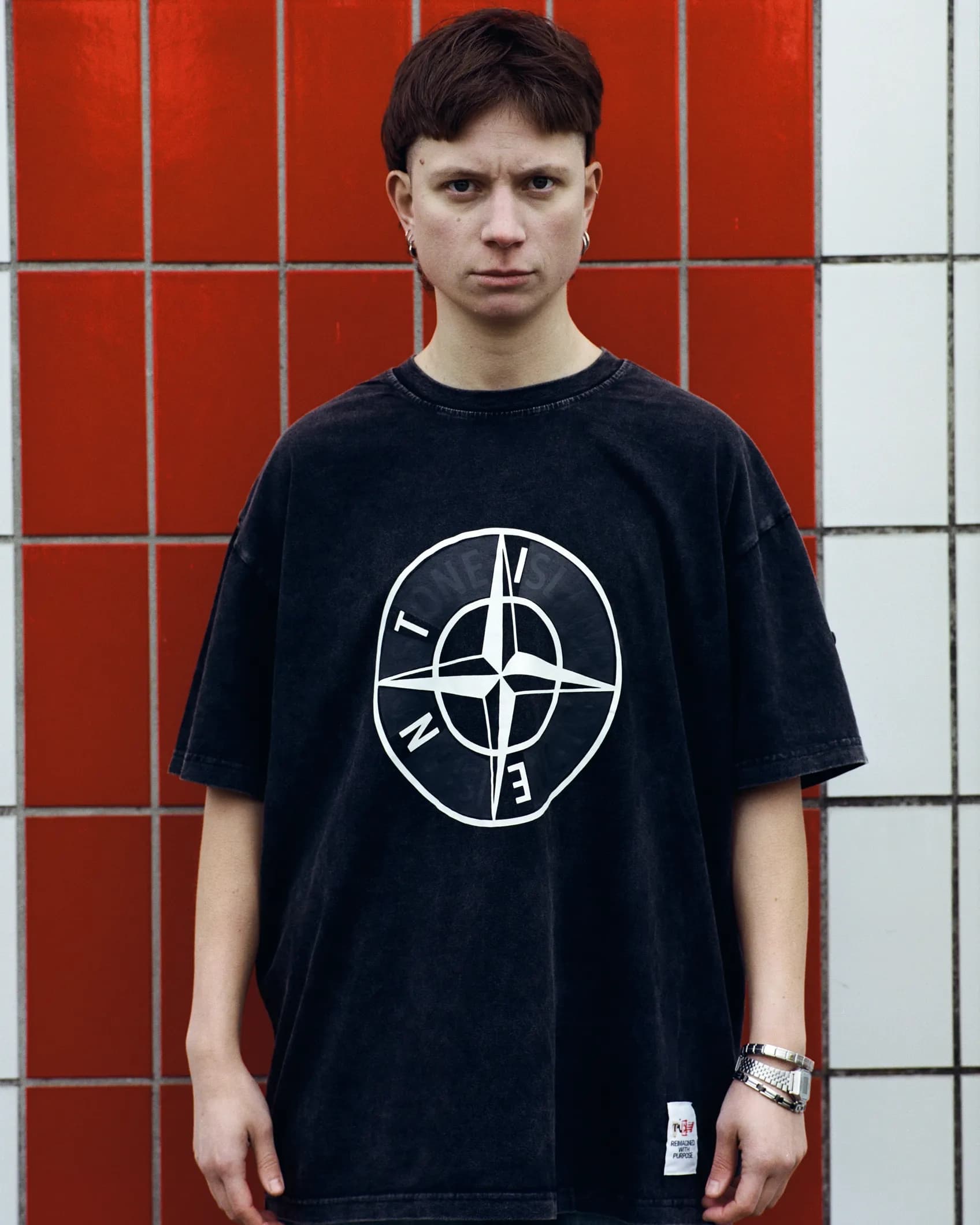 Close-up of a washed black t-shirt with the Stone Island compass logo reworked to read TIEN, keeping the original circular badge layout intact.