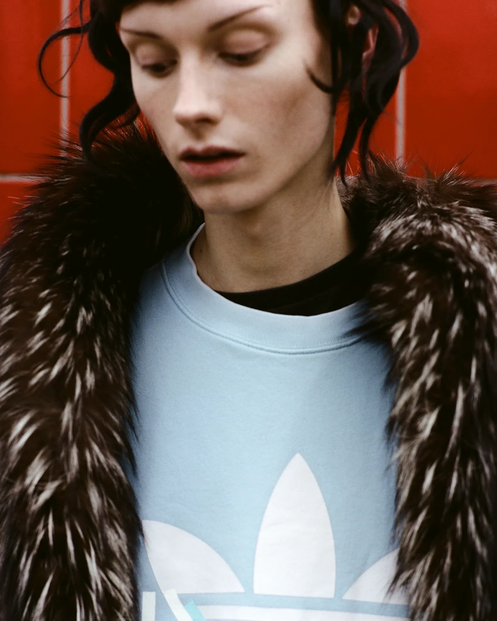 Close-up of a person wearing a plain light blue sweatshirt layered under a fur coat, shot for the TIEN campaign
