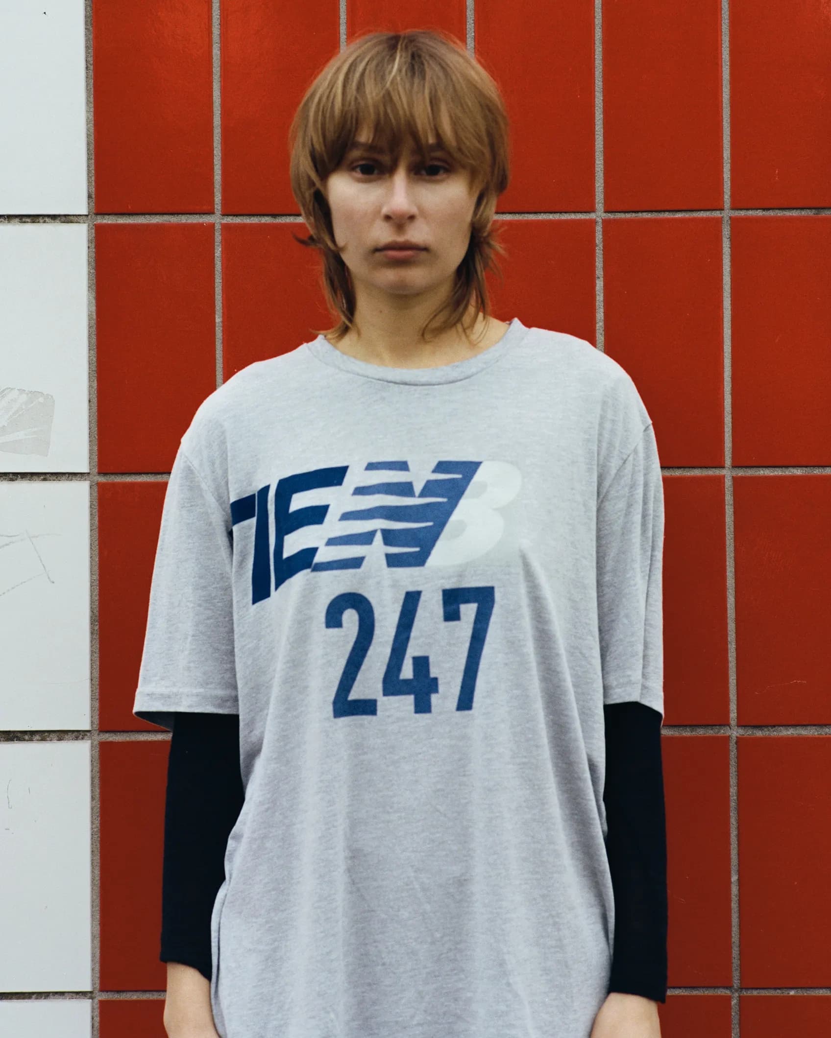 Close-up of a grey New Balance 247 long-sleeve shirt with the brand name replaced by TIEN, keeping the original logo layout and typography intact.