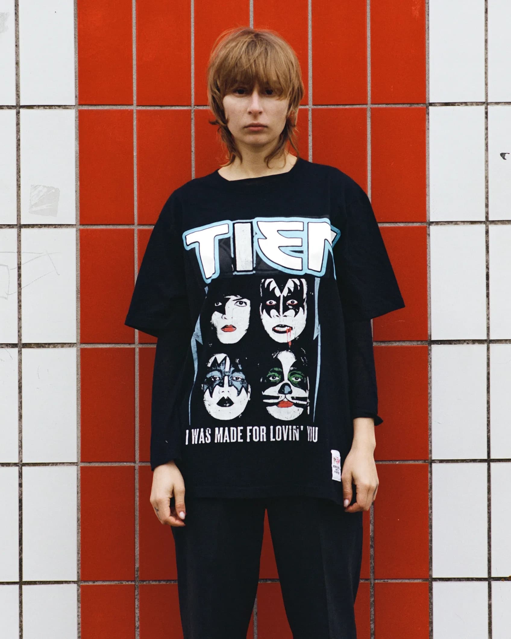 Close-up of a vintage Kiss band t-shirt with the band name replaced by TIEN in the original heavy metal lettering style, keeping the four band member portraits intact.