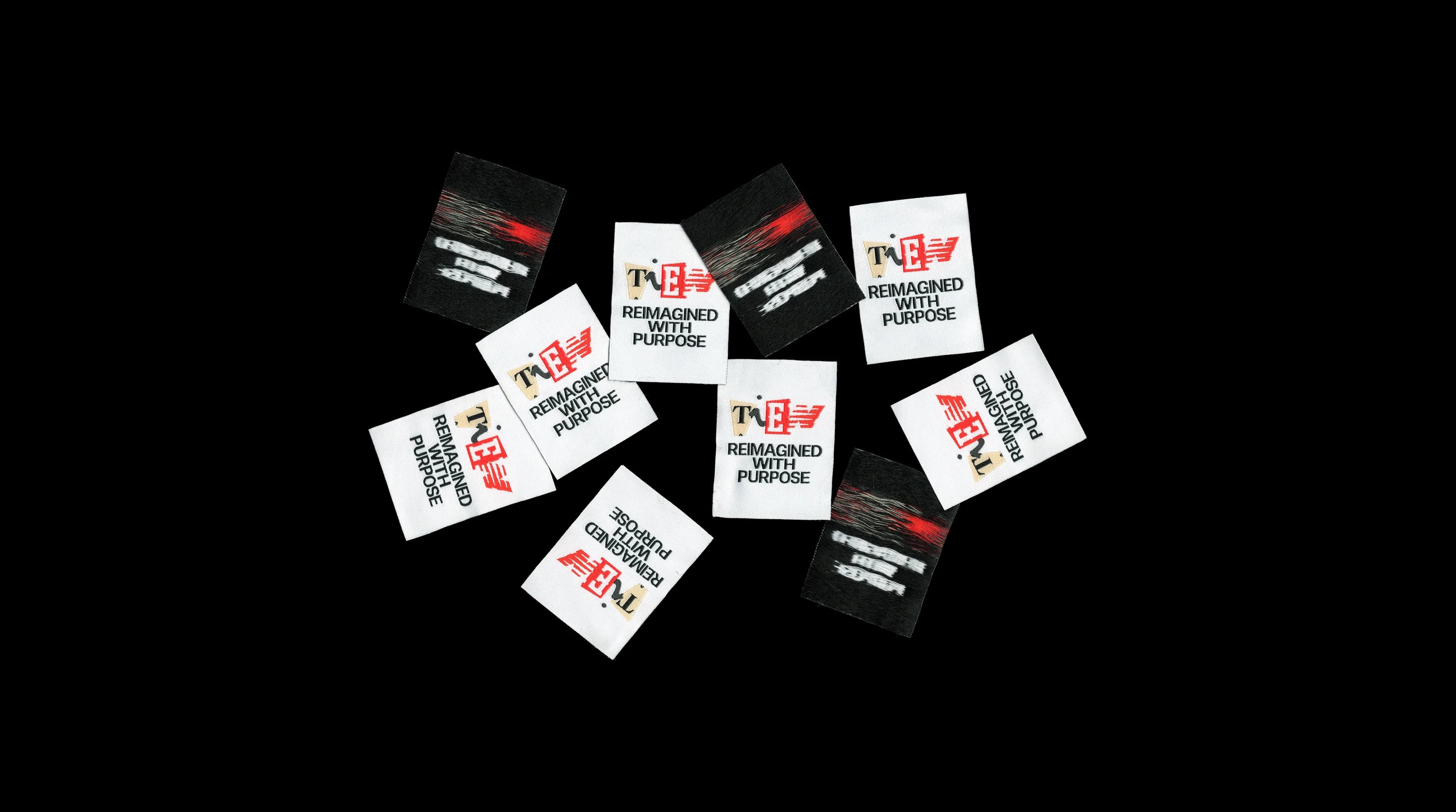 Scattered woven clothing labels printed with the TIEN wordmark and the tagline "Reimagined With Purpose", used to rebrand the vintage garments in the TIEN collection.