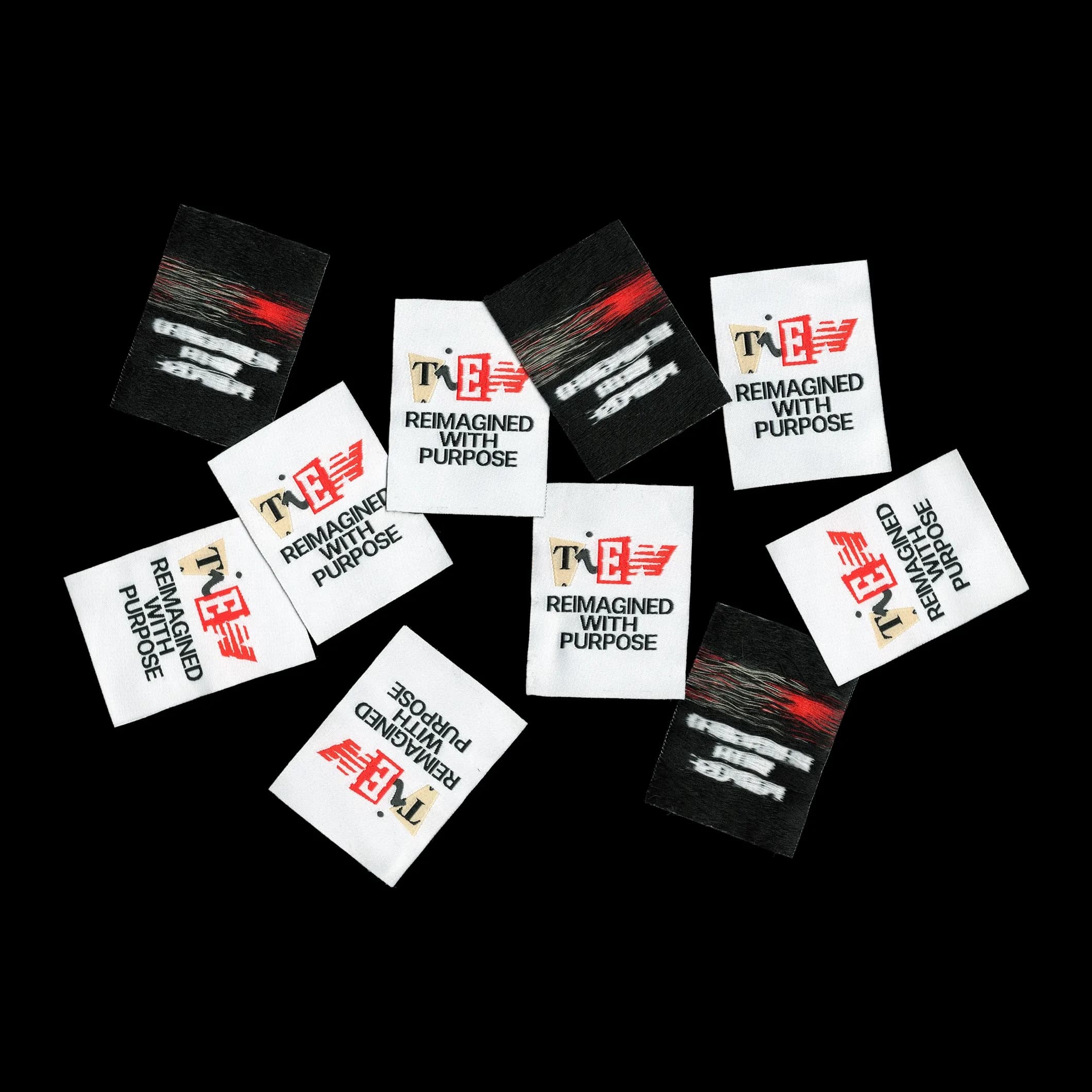 Scattered woven clothing labels printed with the TIEN wordmark and the tagline "Reimagined With Purpose", used to rebrand the vintage garments in the TIEN collection.