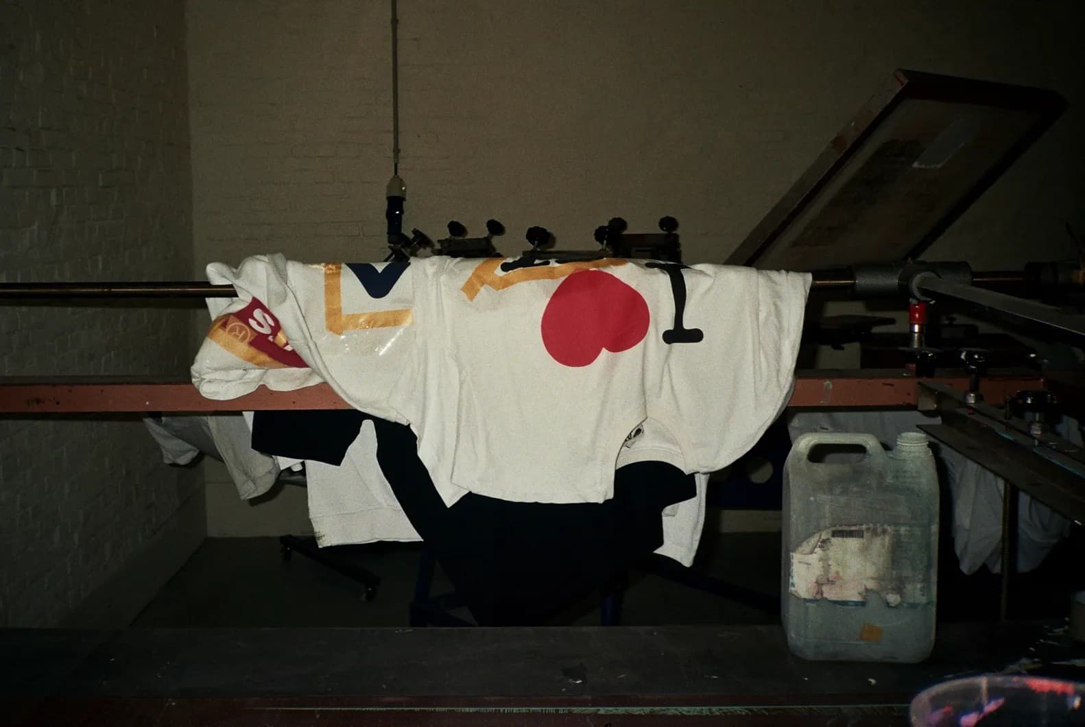 Behind the scenes shot of a freshly printed TIEN t-shirt hanging to dry on the silkscreen press, showing the "I ♥ TIEN" print.