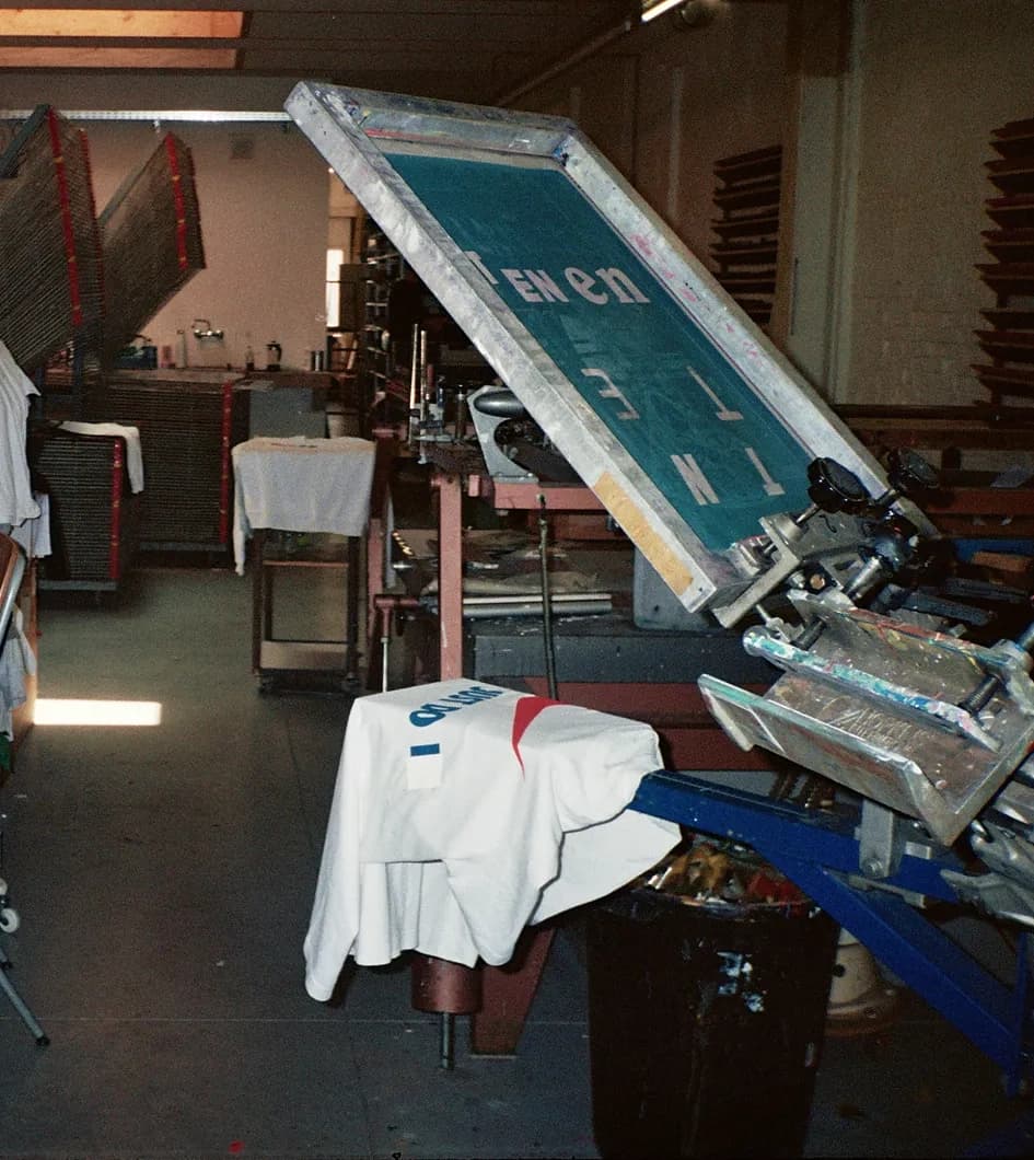 Behind the scenes shot of the silkscreen print shop with a TIEN screen lifted on the press and a vintage Lacoste t-shirt loaded underneath, ready to be reworked.