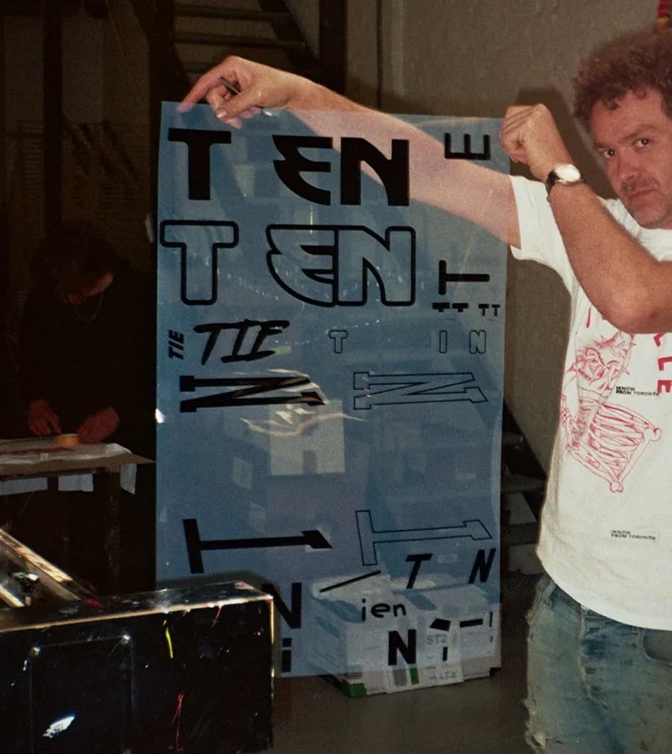 Behind the scenes close-up of a silkscreen with multiple TIEN letterform variations cut into it, showing the different letter sources laid out across a single screen ready for printing.