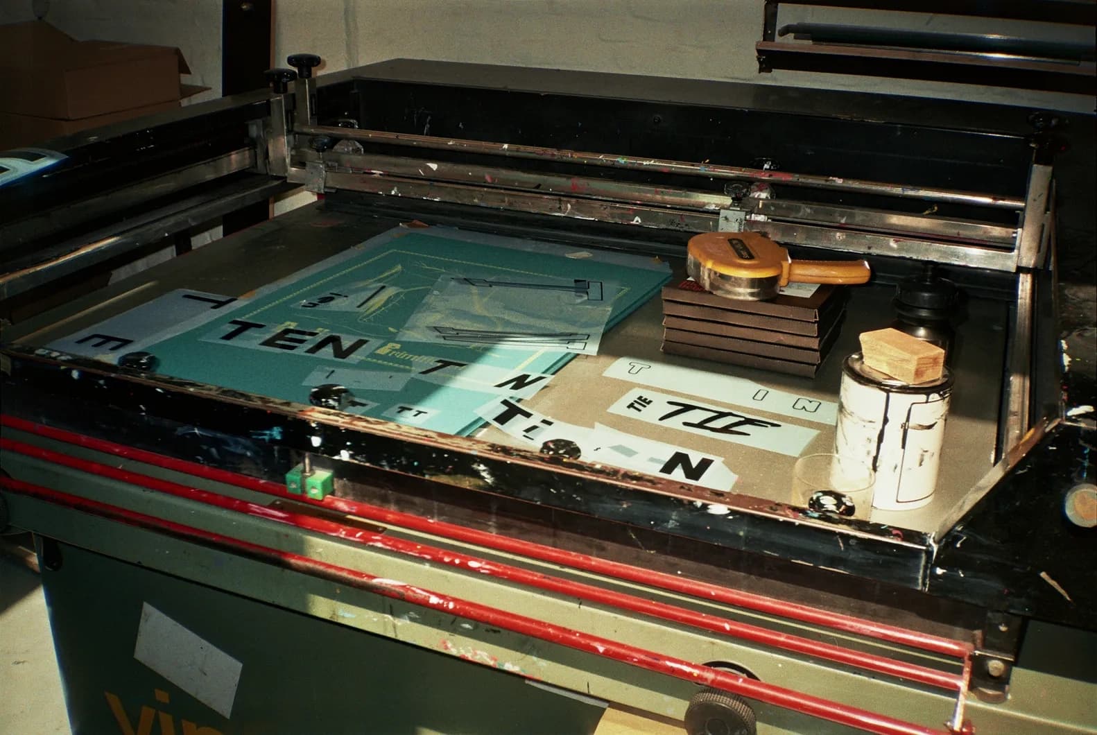 Behind the scenes shot of multiple TIEN silkscreen frames laid out on a print table, each carrying different letterform combinations, with ink tins and tools alongside.